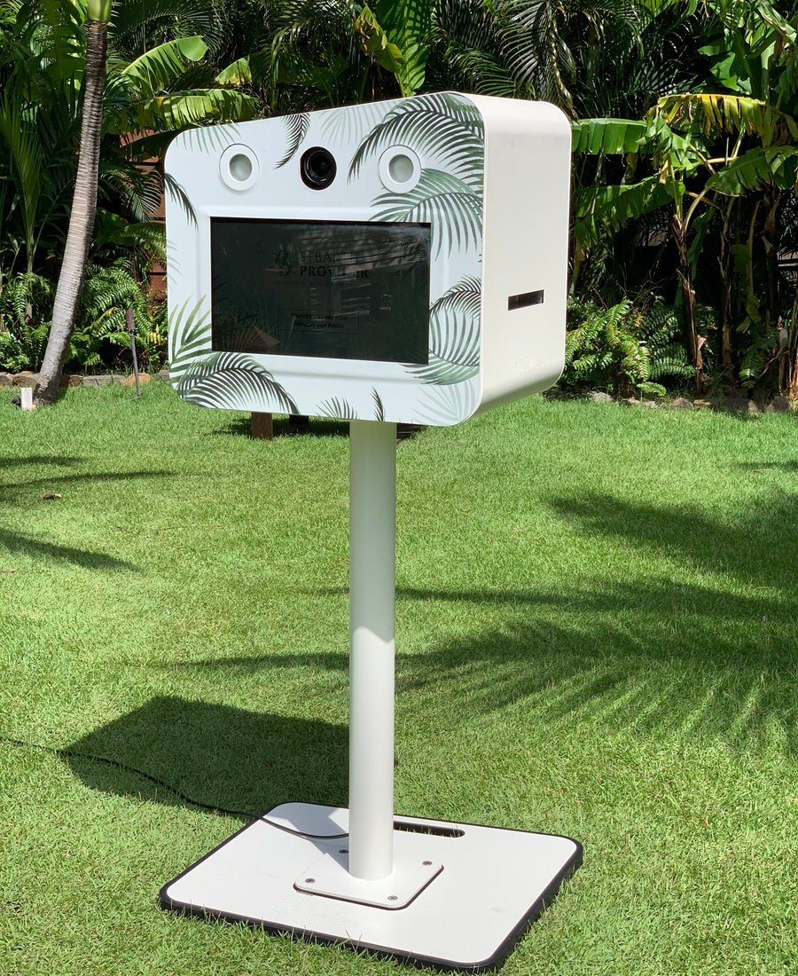 Photobooth blanc à motif palmes installé dans un jardin tropical